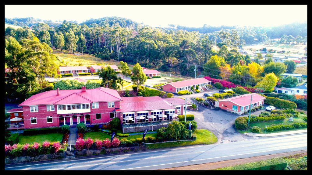 Kermandie hotel and Lodge. Image of large building with a number of smaller buildings cascading up a slope. Forest and mountains behind.